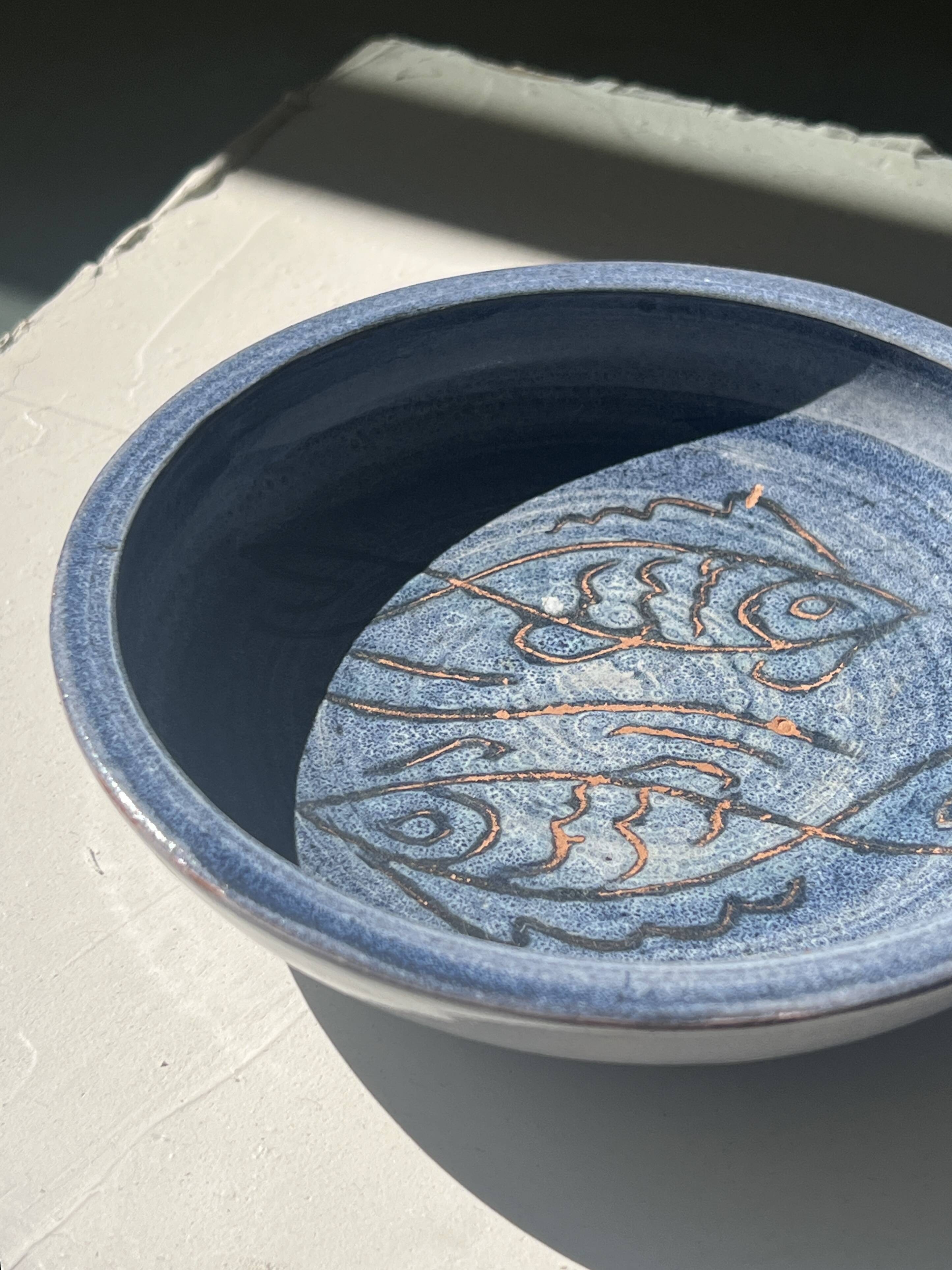 Glazed blue ceramic bowl with stylised fish decoration.