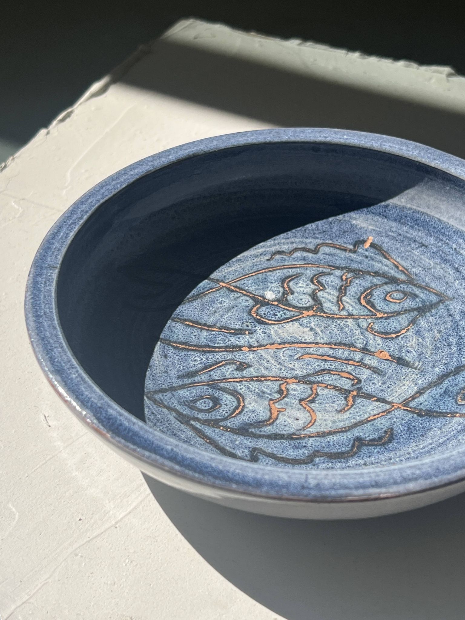 Glazed blue ceramic bowl with stylised fish decoration.