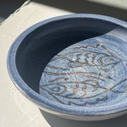 Glazed blue ceramic bowl with stylised fish decoration.