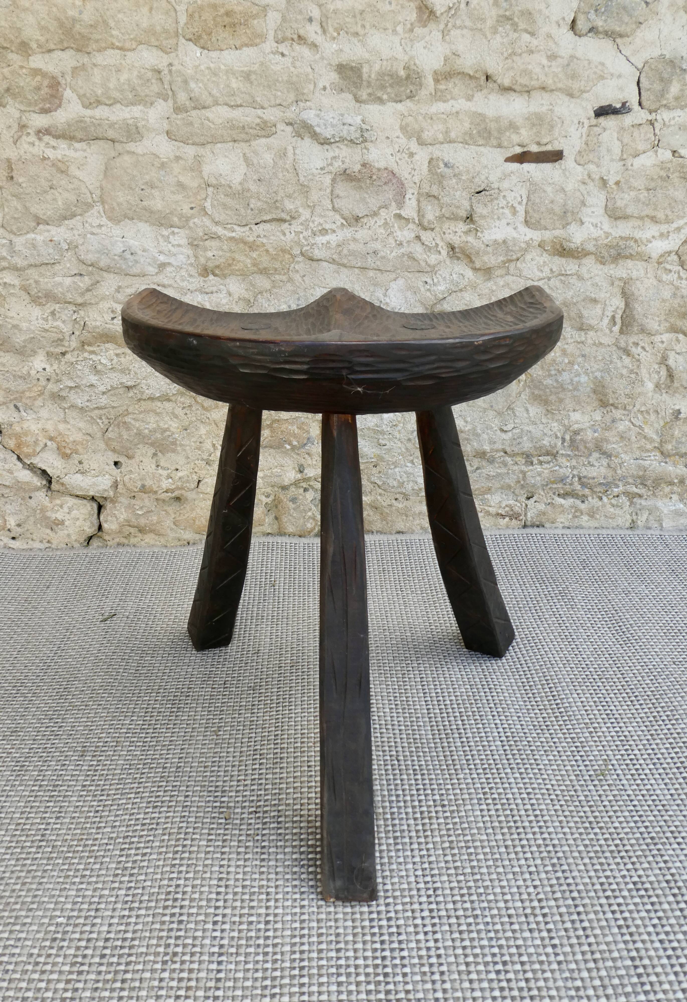 Tripod stool made of solid wood, with a carved seat.