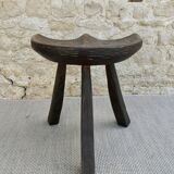 Tripod stool made of solid wood, with a carved seat.