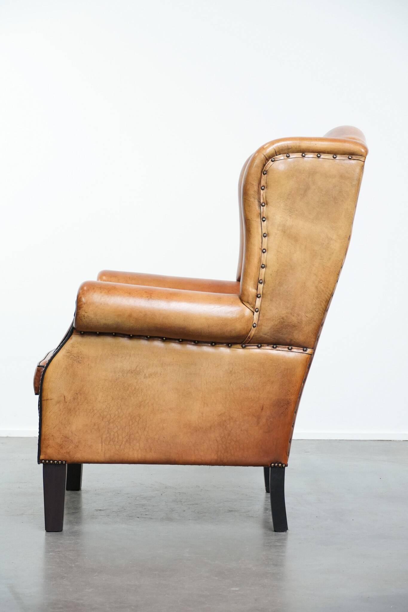 Large sheepskin wingback chair with black piping and decorative nails