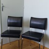 Chrome metal chairs and black faux leather upholstery in retro modernist style.