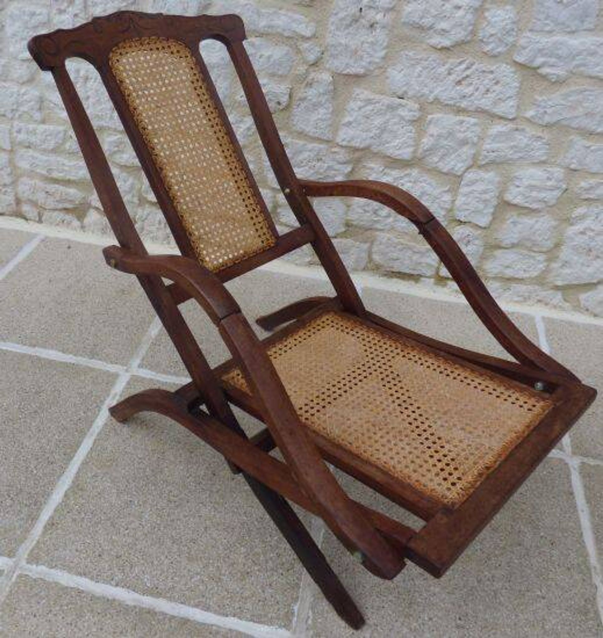 Antique folding chair with caned seat and backrest made of wood.