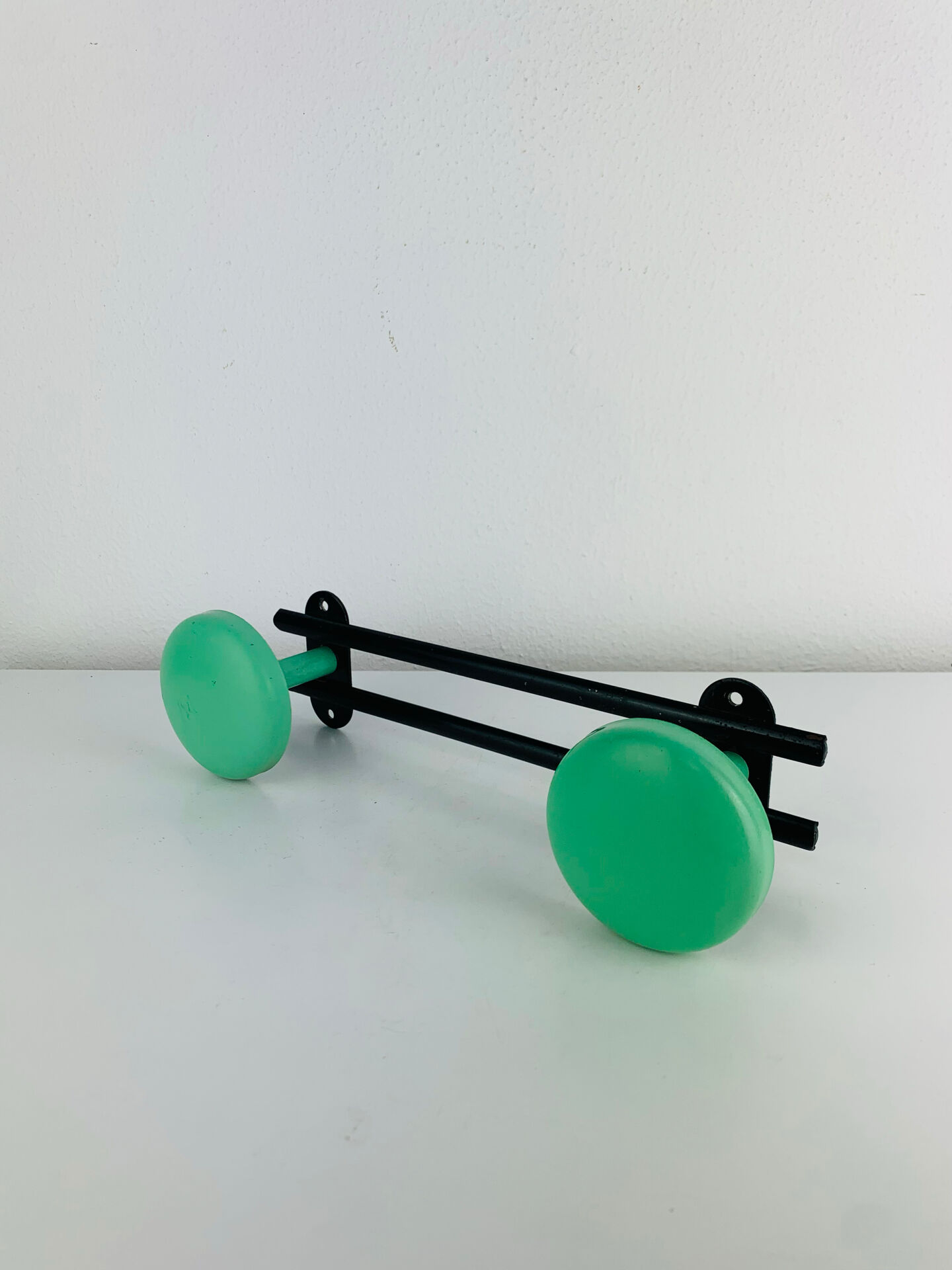 Wall-mounted coat rack with 2 green hooks from the 1950s.
