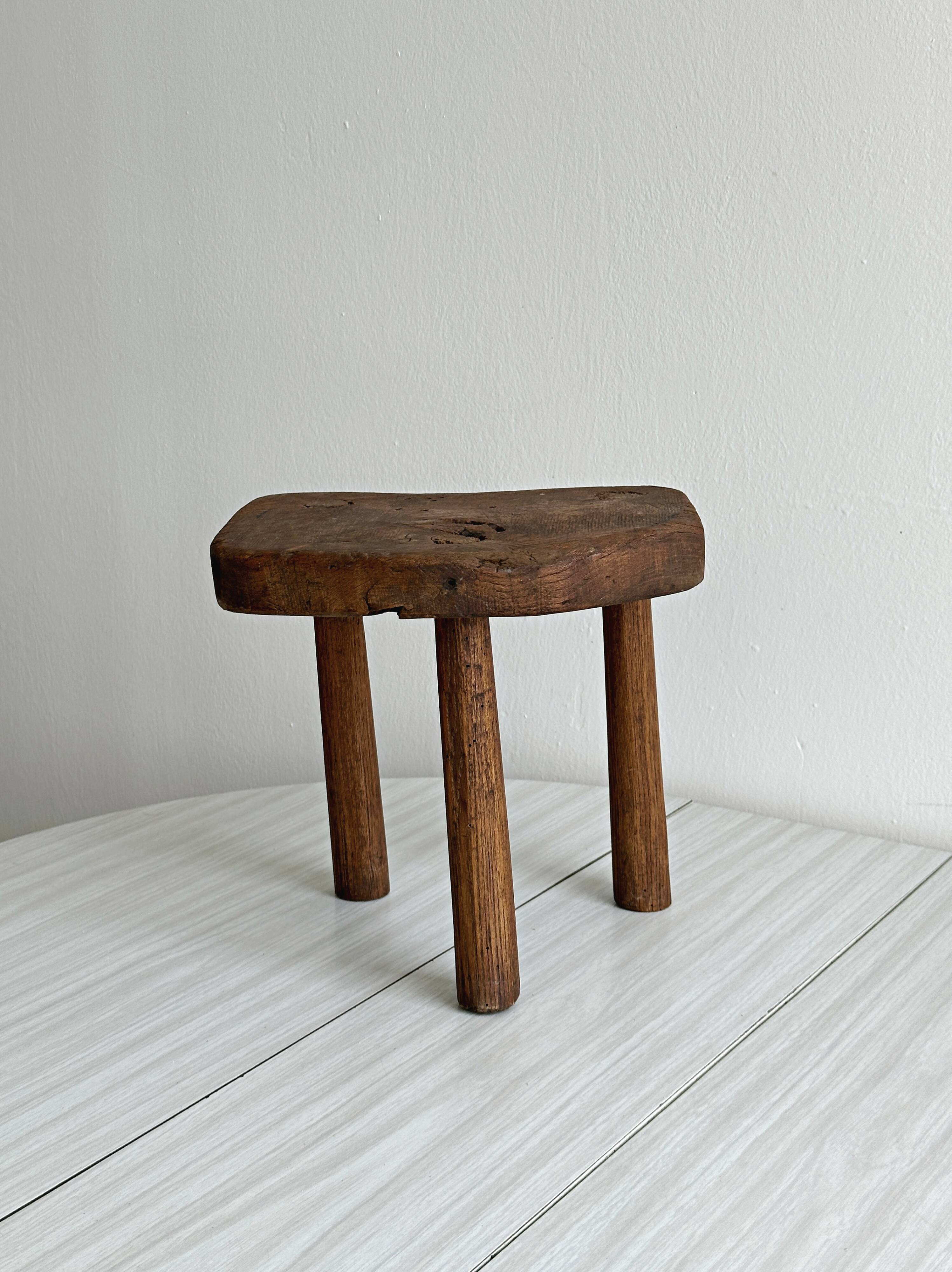 Antique three-legged stool made of raw solid wood.