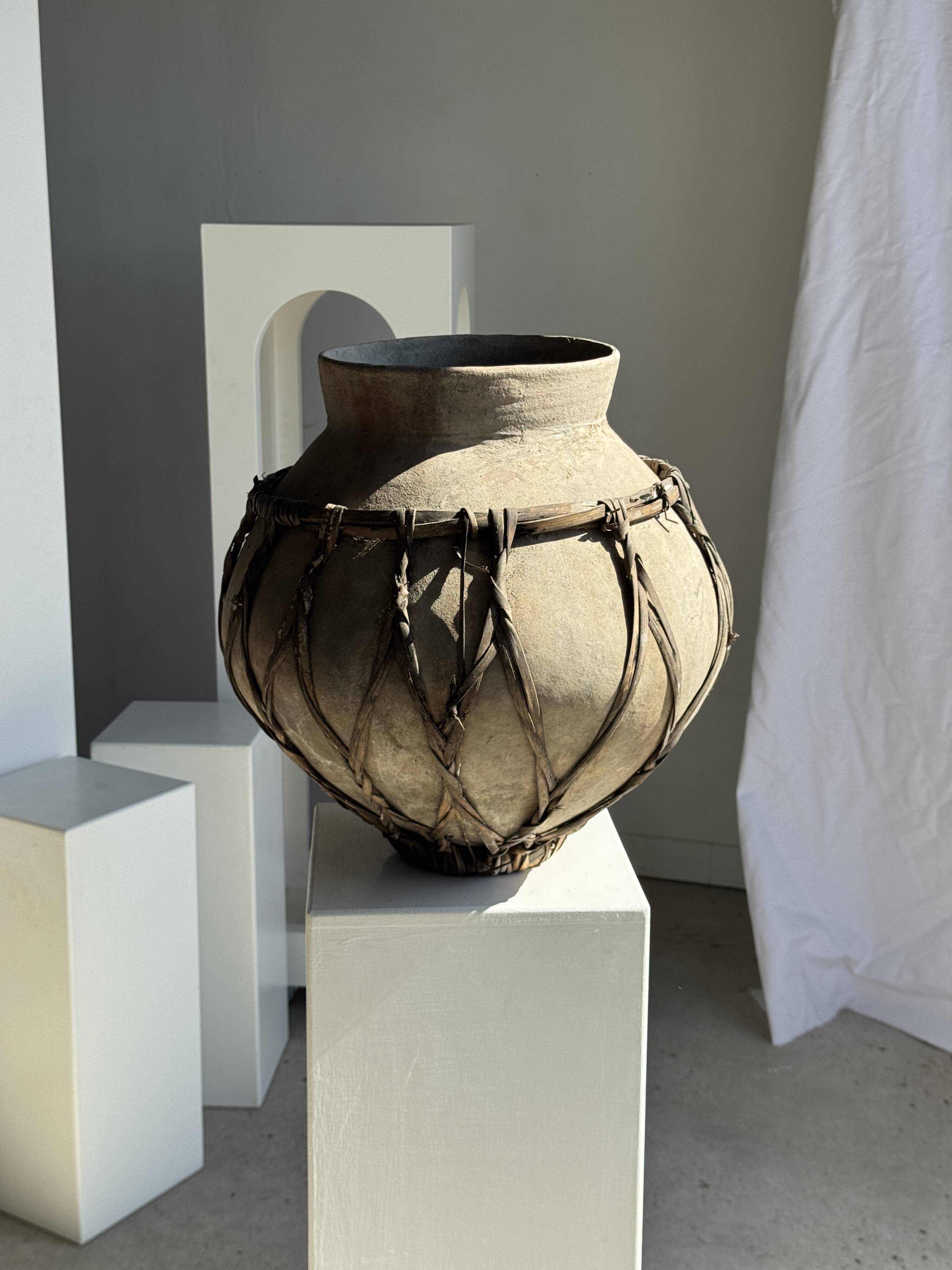 Very large light grey terracotta pot with handles and rattan crossbars.