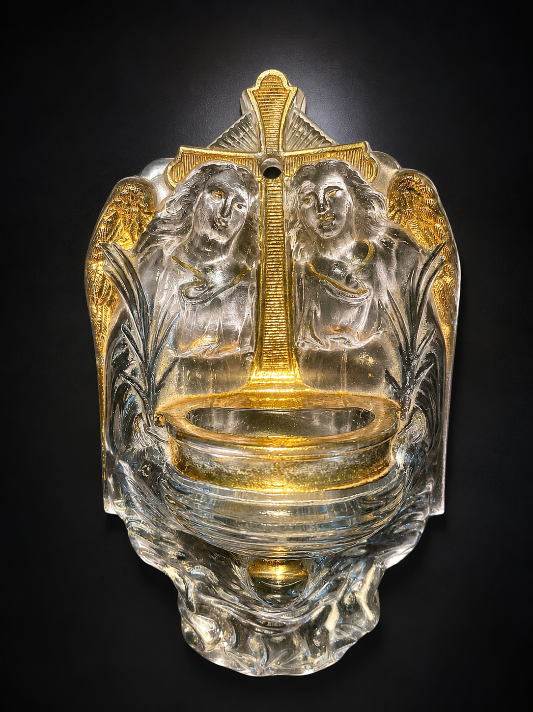 Old wall-mounted holy water font in moulded glass decorated with angels.