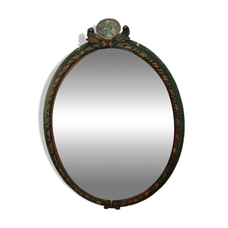 Antique oval mirror in a carved and painted frame with a floral panel.