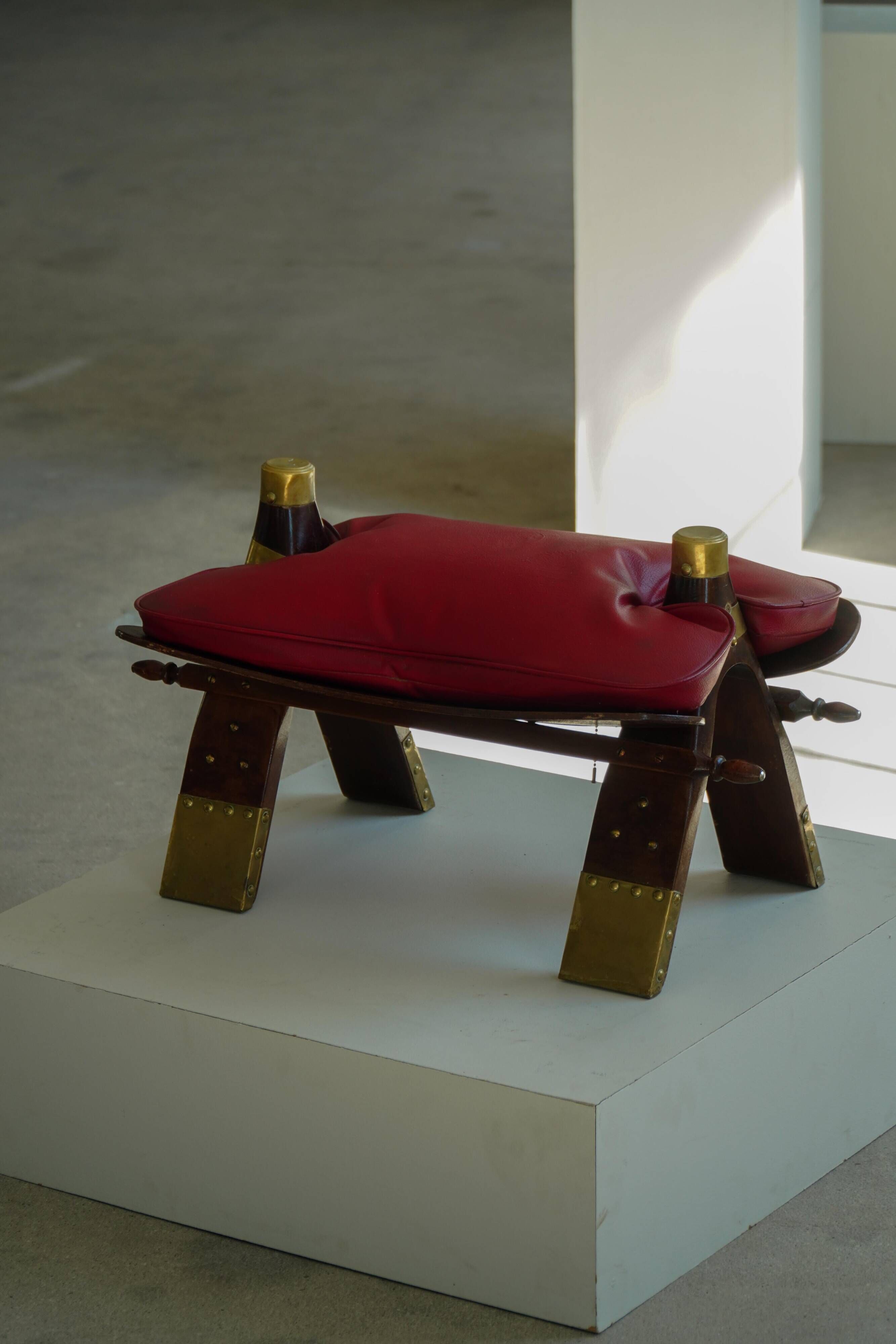 Moroccan stool in the shape of a camel saddle, stained wood, brass and leather, North Africa, 1980.