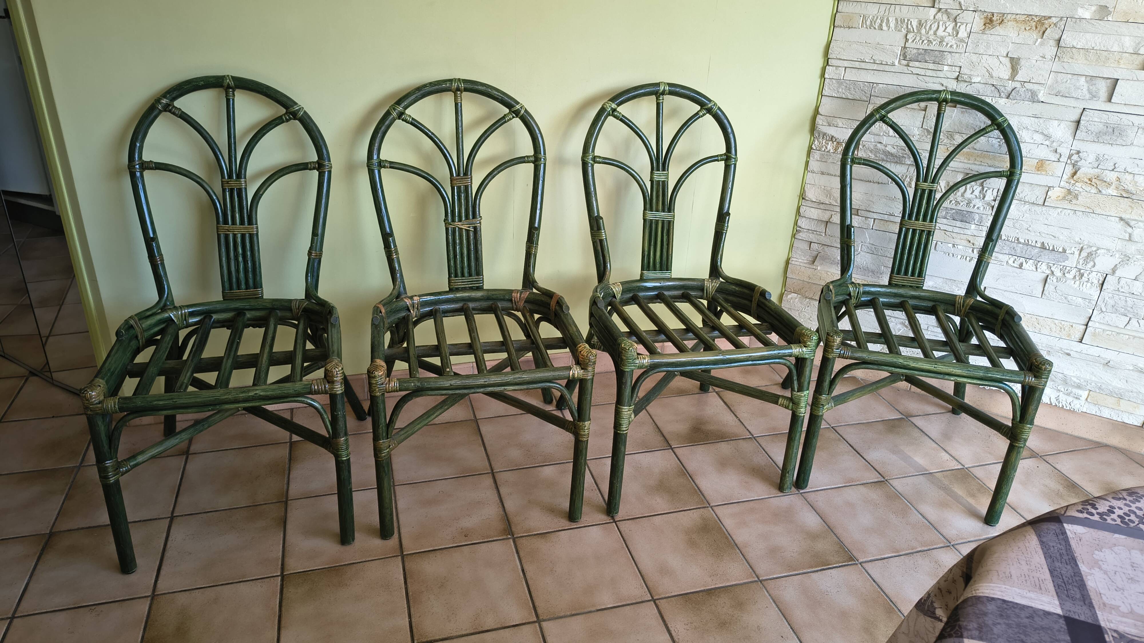 Round rattan table with glass top and 4 green rattan chairs.