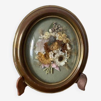 Old medallion frame in curved glass with a composition of dried flowers