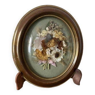Old medallion frame in curved glass with a composition of dried flowers