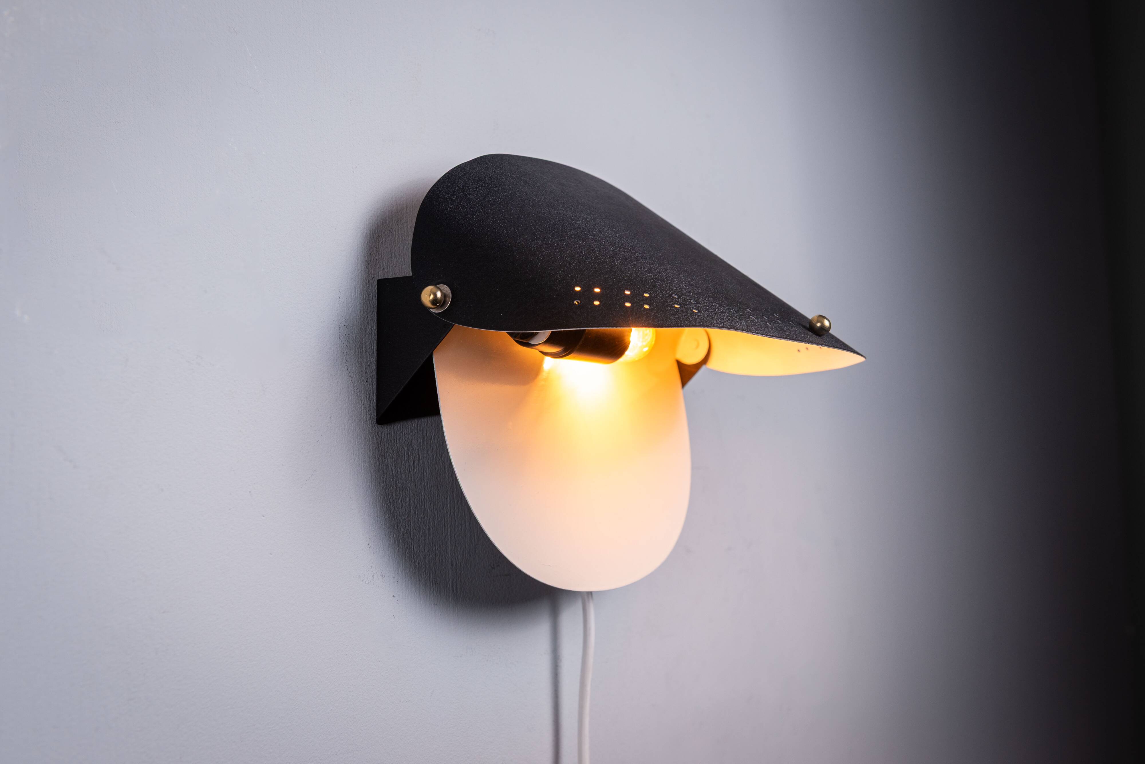 Matte black wall lamps with perforated shades and brass details