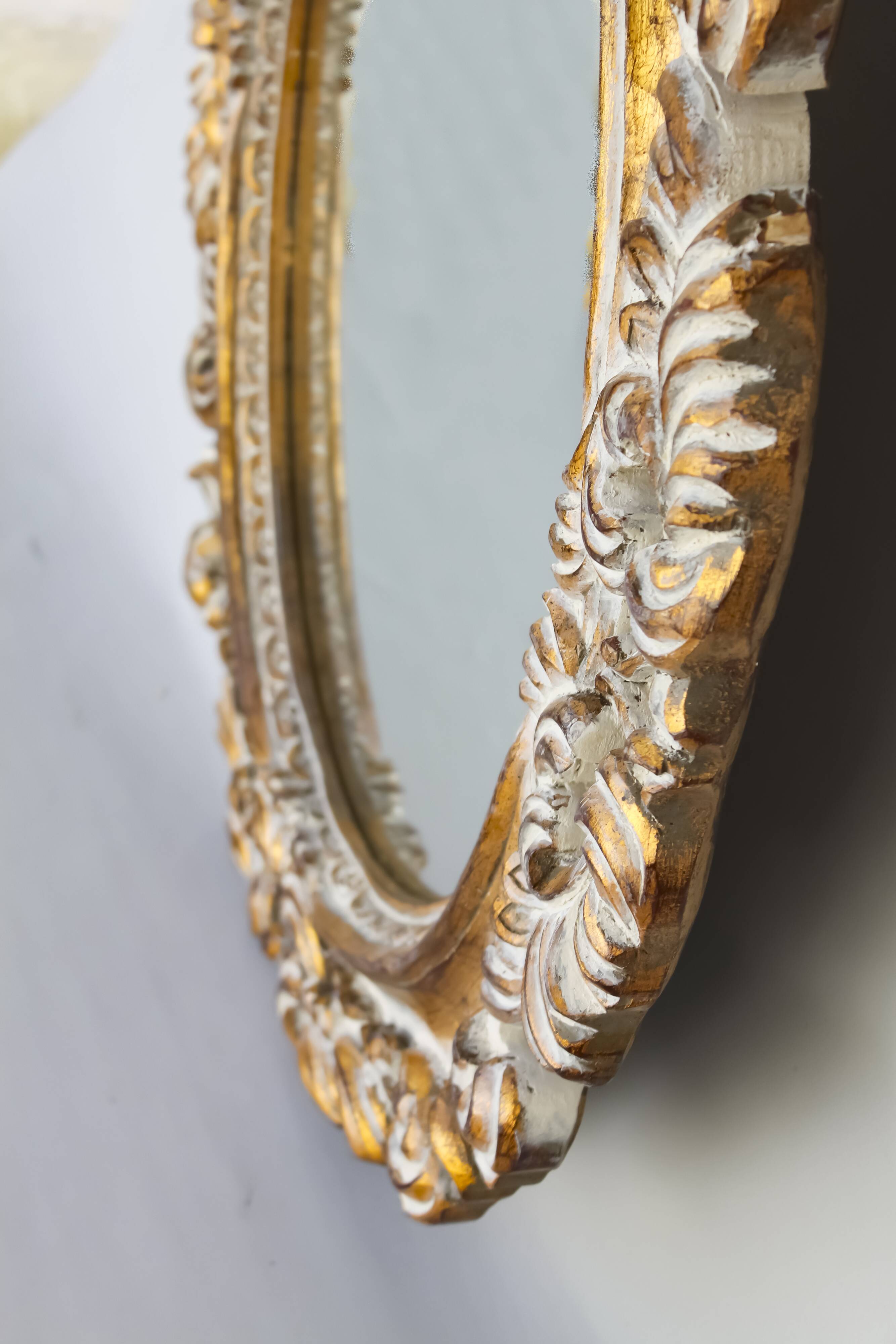 Distressed and carved golden oval mirror in wood.