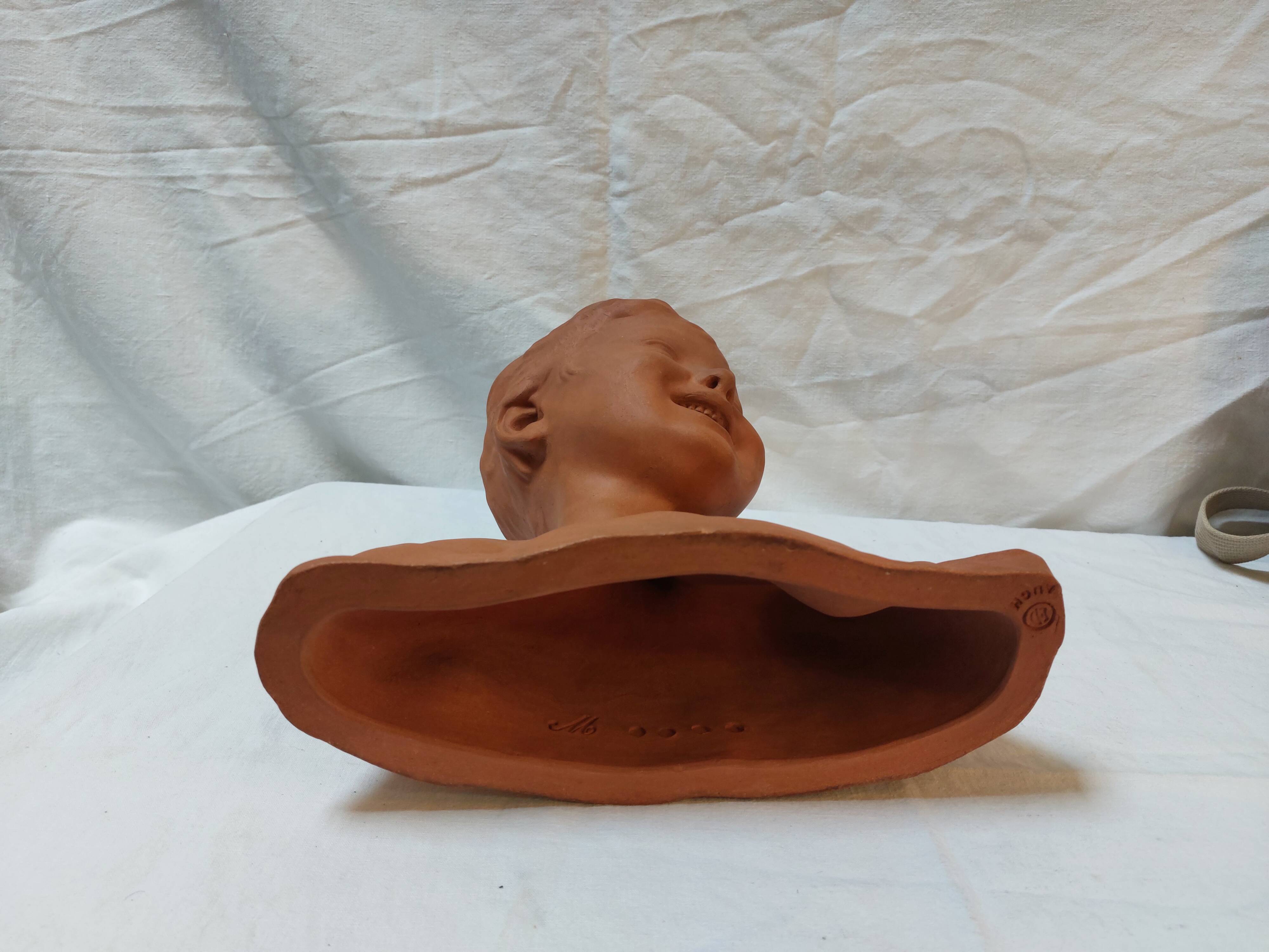 Terracotta bust of a smiling little boy.