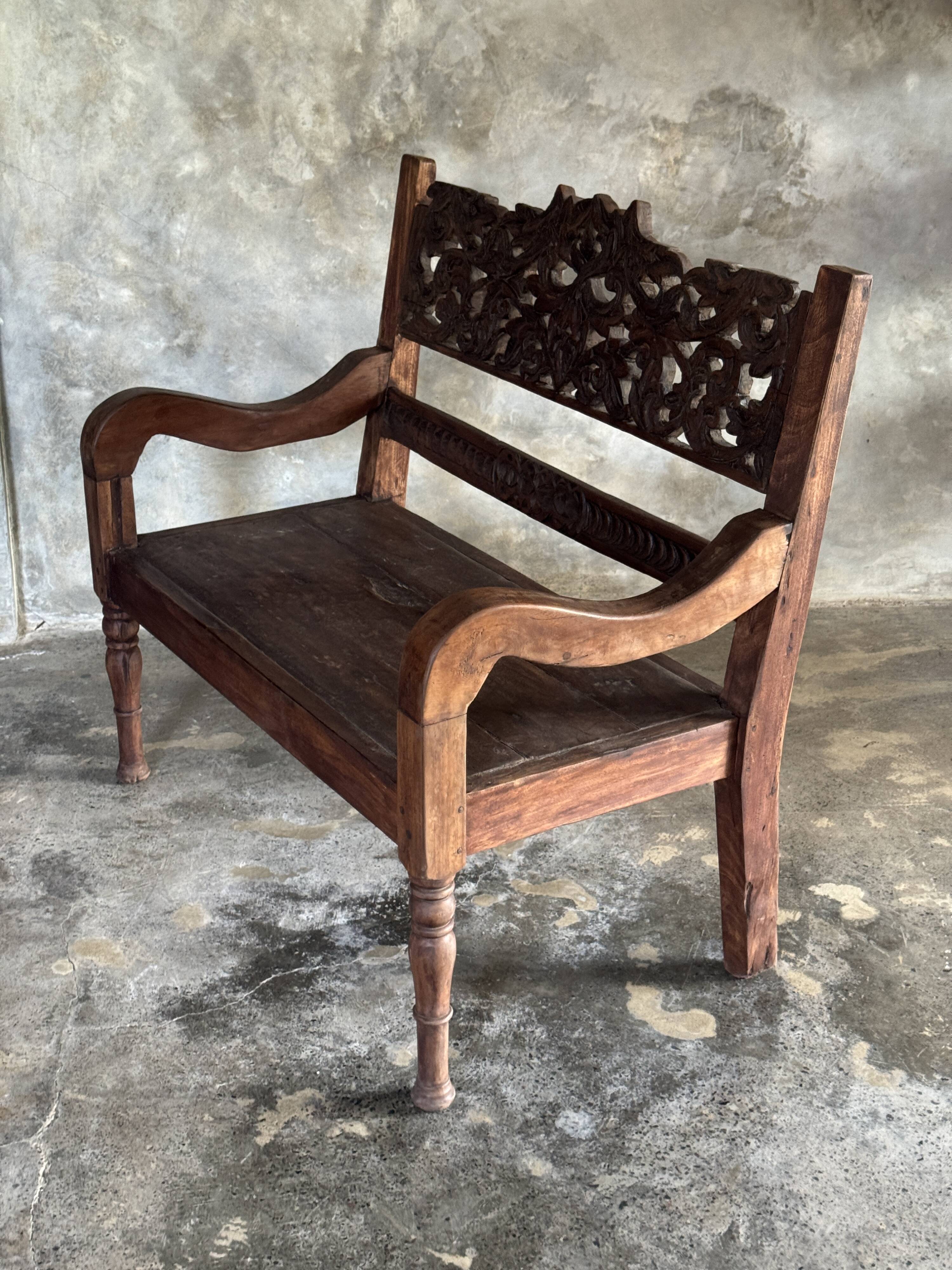 Small antique Indonesian bench in carved teak with plant and floral motifs.