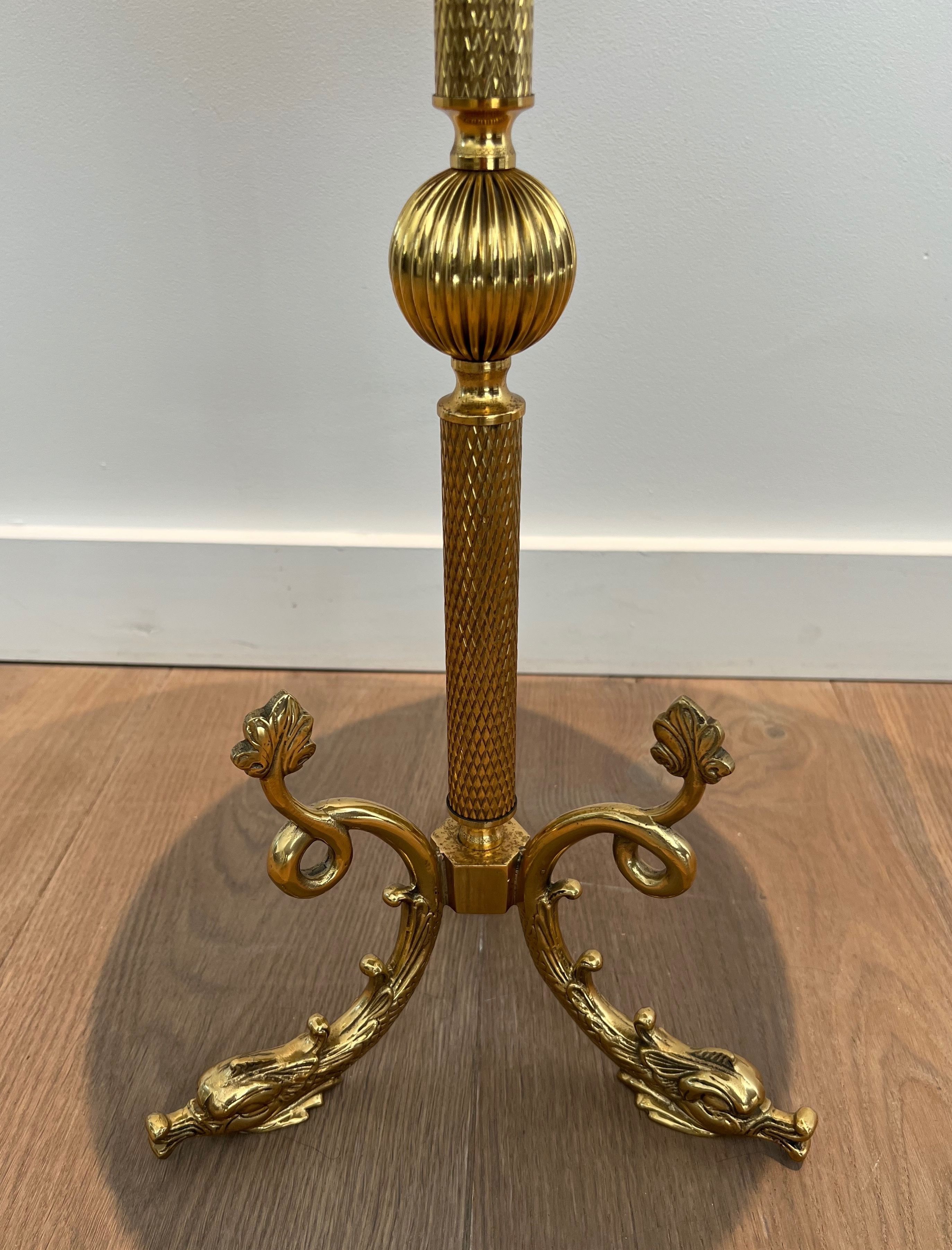 A round, neoclassical-style brass side table with a base decorated with dolphins and a red celluloid top encircled by an openwork gallery, attributed to the House of Jansen.