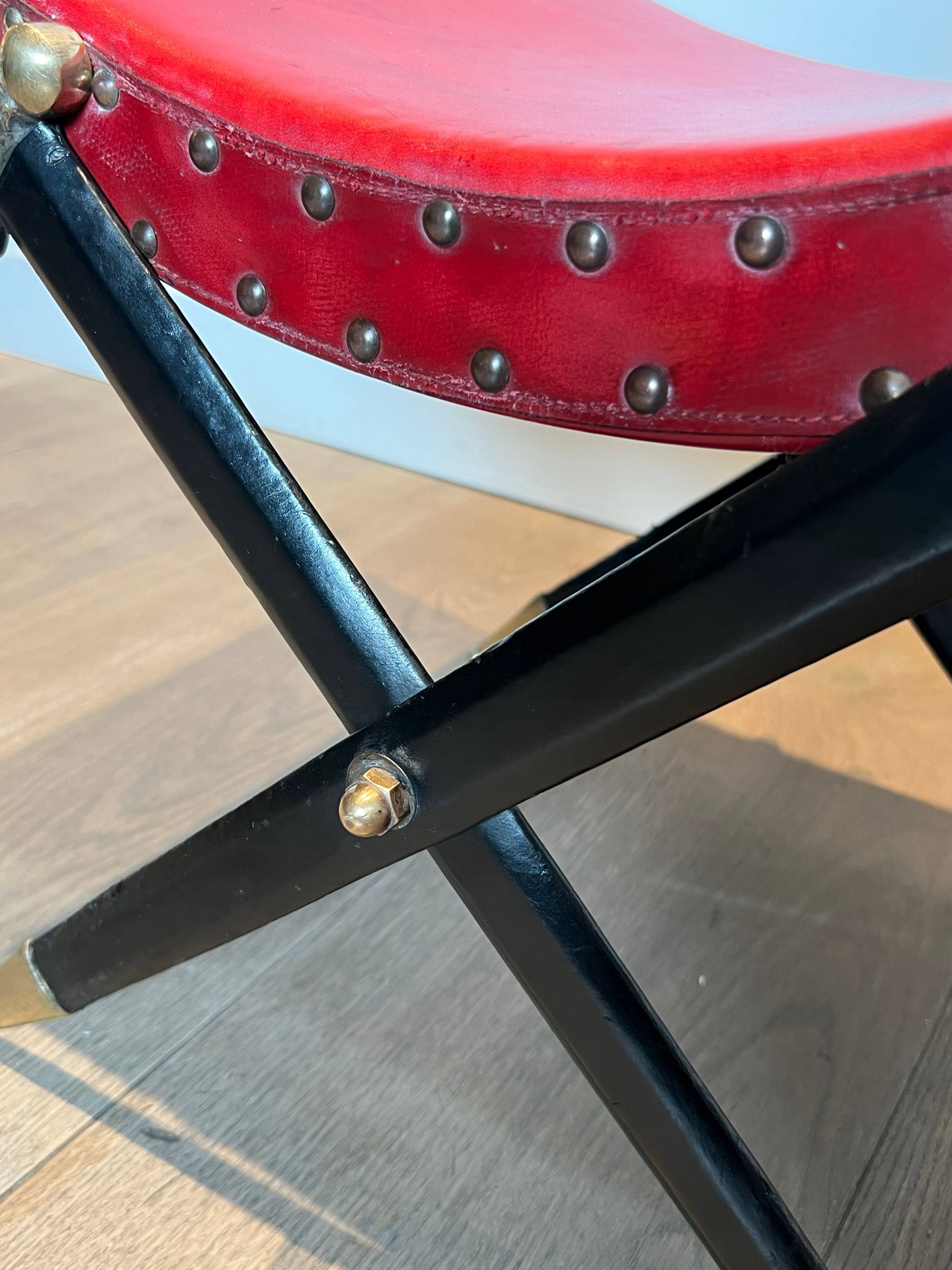Neoclassical curule stool in red leather, decorated with crossed swords in bronze and metal covered in black leather.