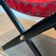 Neoclassical curule stool in red leather, decorated with crossed swords in bronze and metal covered in black leather.
