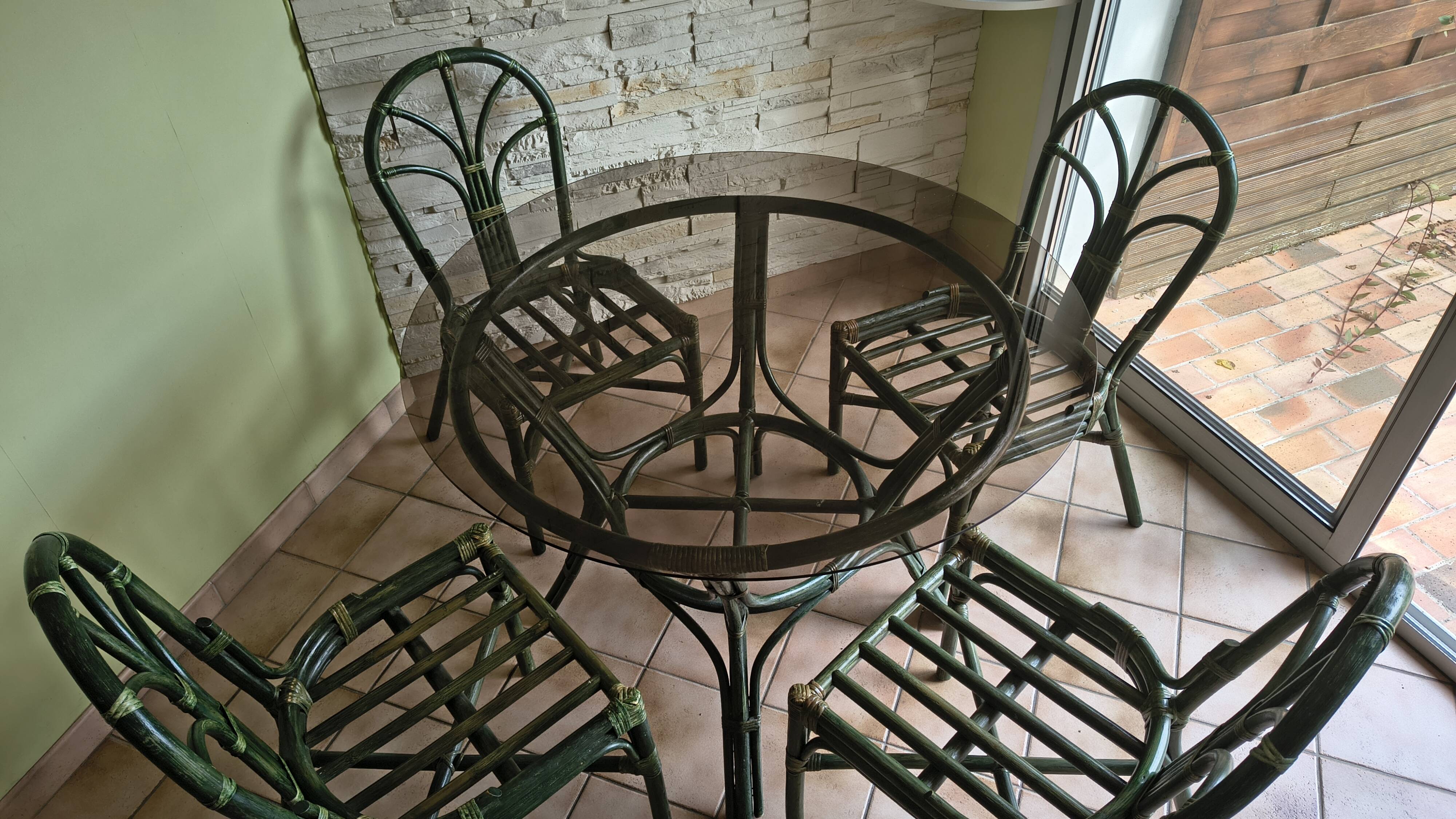 Round rattan table with glass top and 4 green rattan chairs.