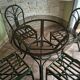 Round rattan table with glass top and 4 green rattan chairs.