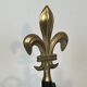Neoclassical-style fire accessory in black lacquered metal and brass with fleur-de-lis.