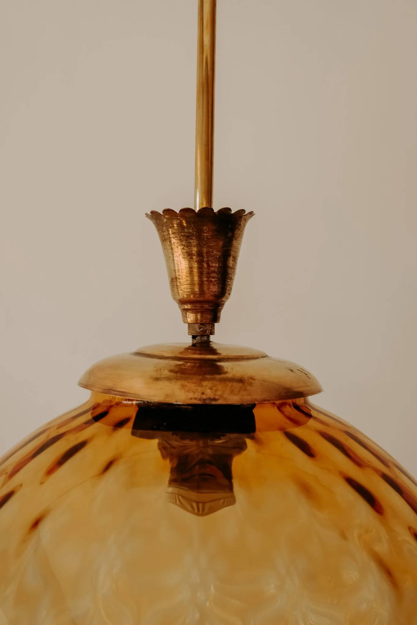 Brass pendant light with a round orange glass shade and a swirling structure.