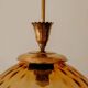 Brass pendant light with a round orange glass shade and a swirling structure.