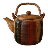 Vintage ceramic teapot with an enamel finish, rattan handle, warm tones.