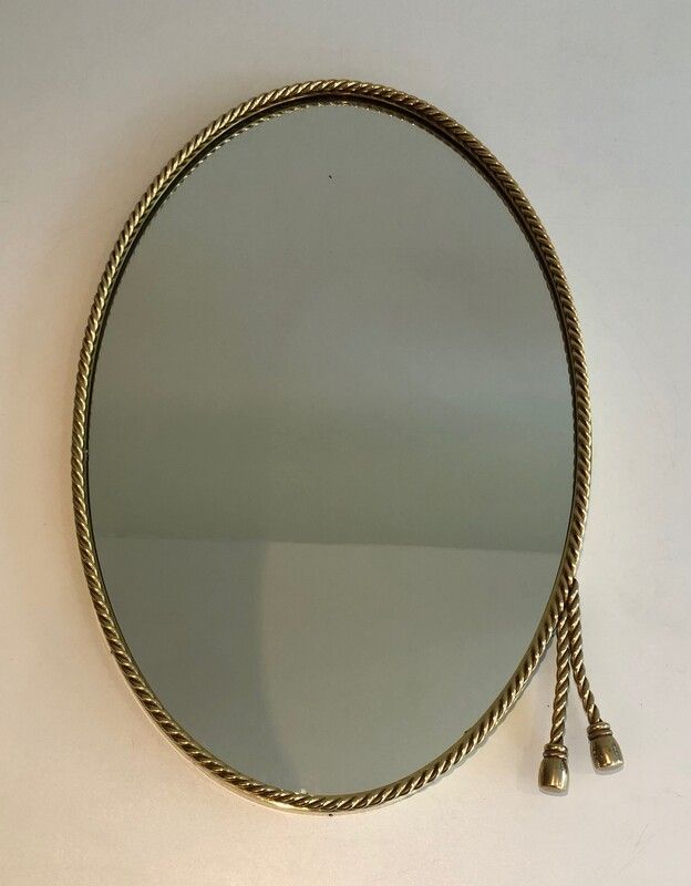 Oval brass mirror surrounded by a cord.