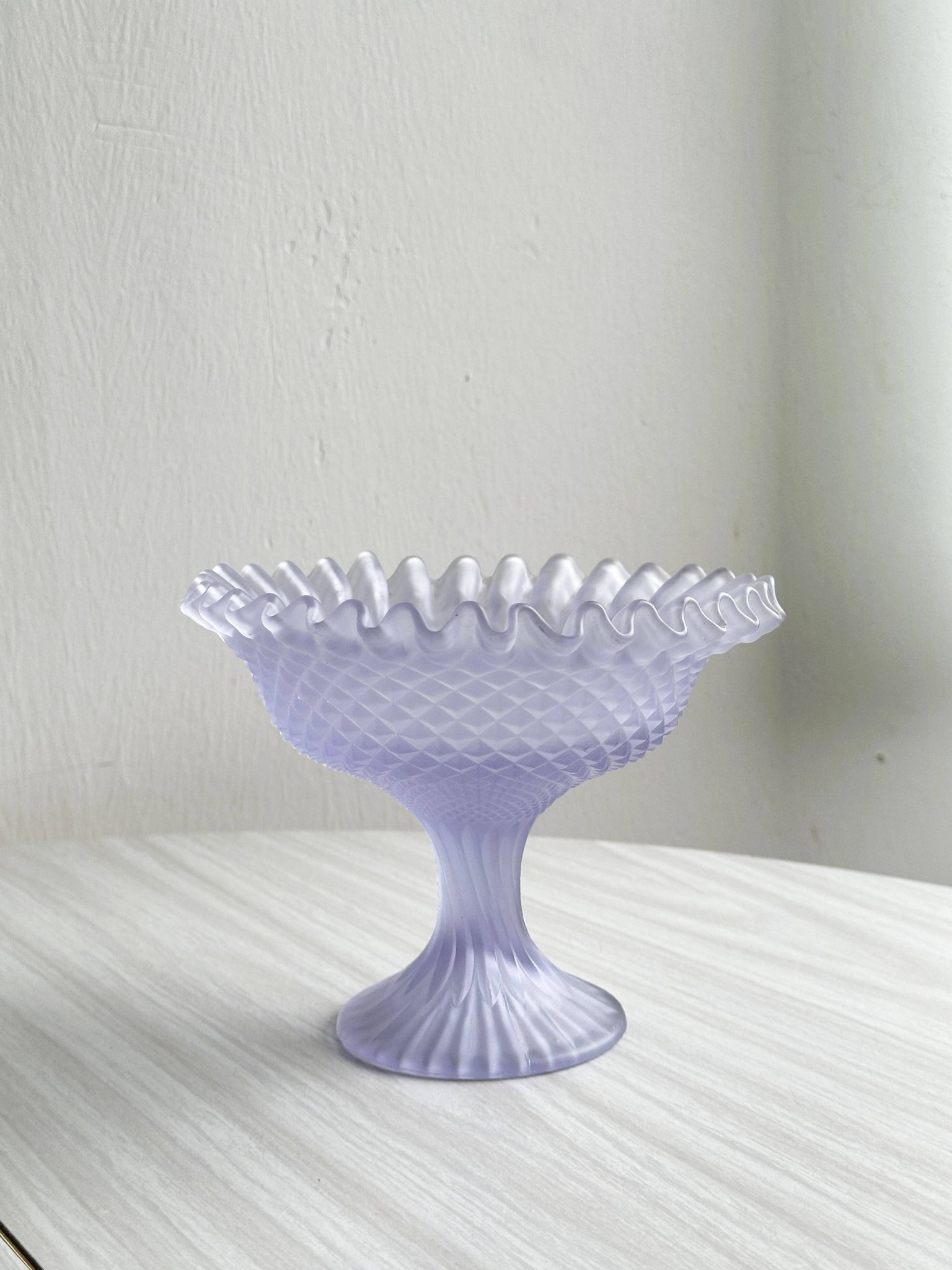 Purple glass pedestal bowl with wavy border and relief pattern.