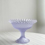 Purple glass pedestal bowl with wavy border and relief pattern.