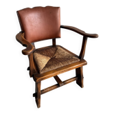 Fauteuil brutaliste en bois massif brun foncé avec assise en rotin naturel et dossier en cuir cognac