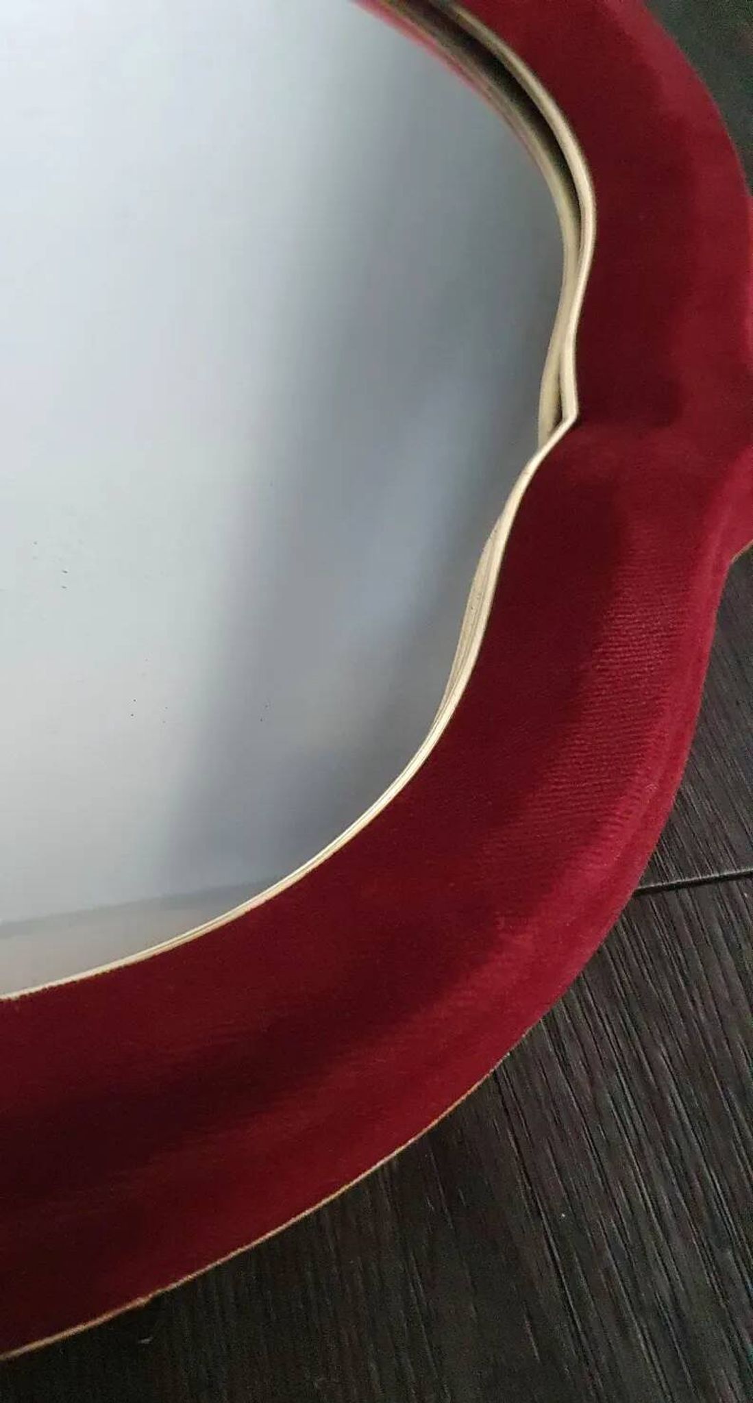 Vintage mirror with a scalloped shape in burgundy velvet and a golden trim.