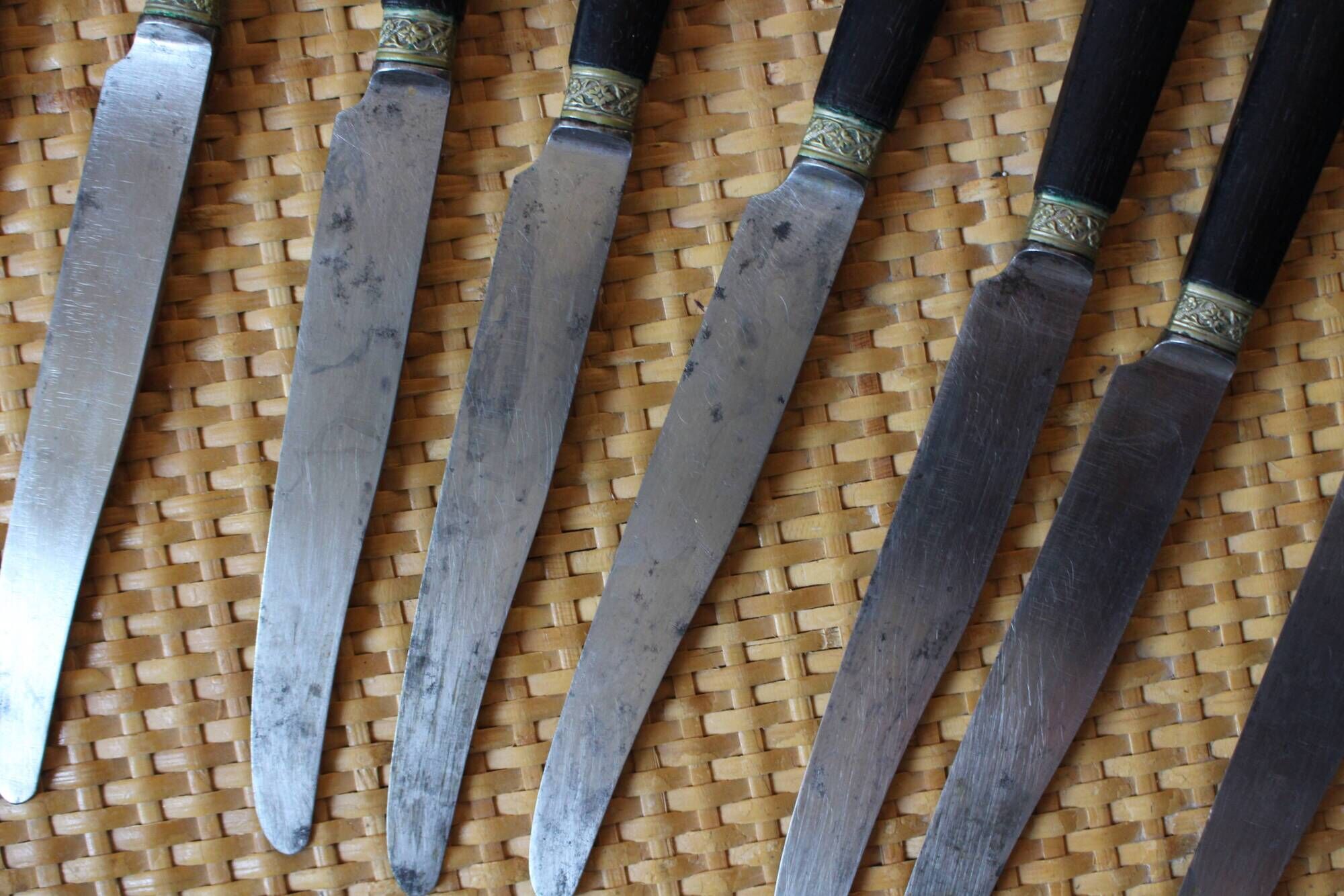 A set of 8 knives with black wooden handles and bolsters.
