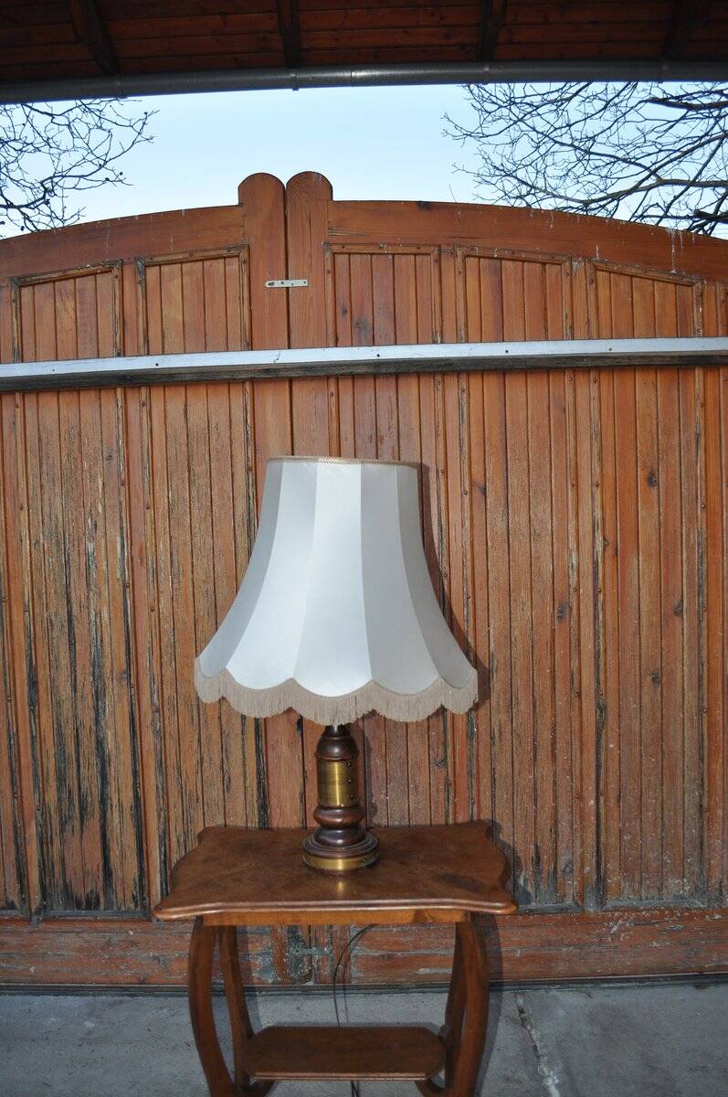 Vintage brown and gold desk lamp made of carved wood and brass, with a fringed shade.