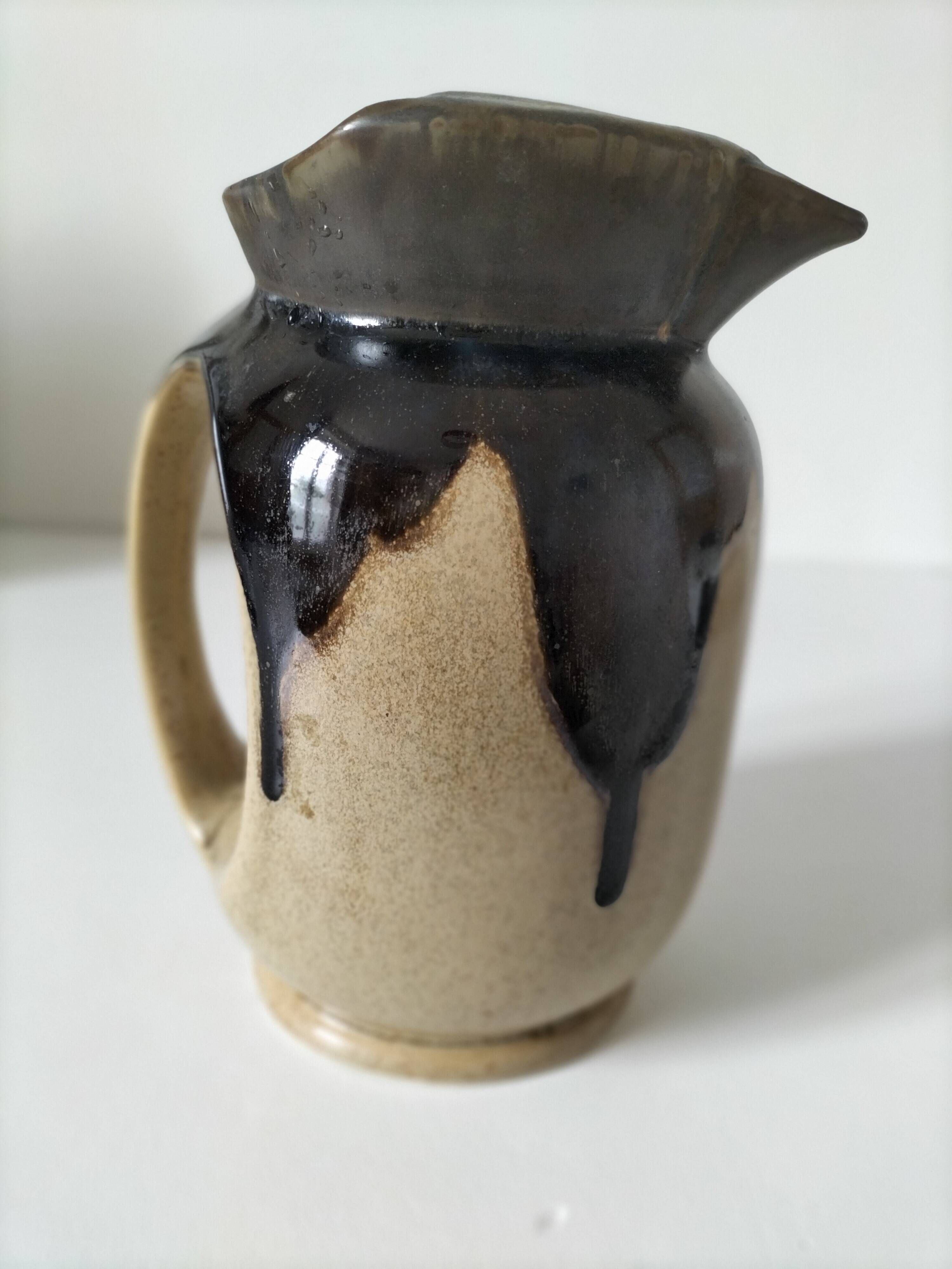 Stoneware jug with deep black drips on a sandy background.