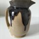 Stoneware jug with deep black drips on a sandy background.