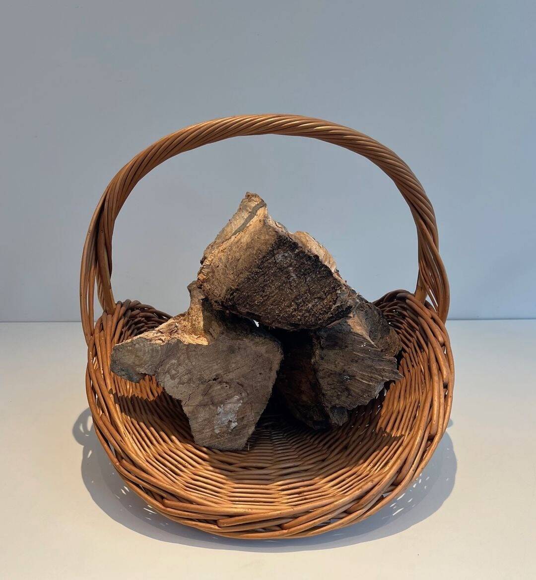 Woven Rattan Log Holder in a Semi-Round Shape with a Central Arched Handle.