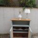 Small vintage green-grey piece of furniture, with 2 doors covered in burlap.