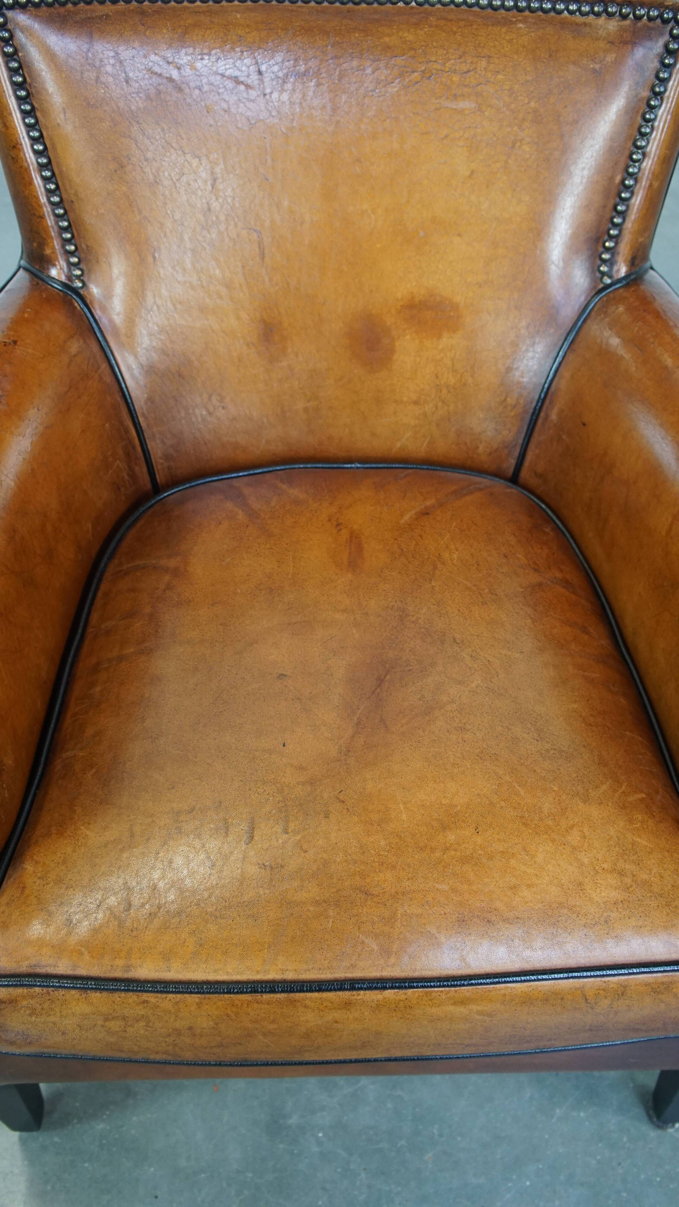 Cognac-colored sheepskin armchair with black piping and decorative nails