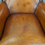 Cognac-colored sheepskin armchair with black piping and decorative nails