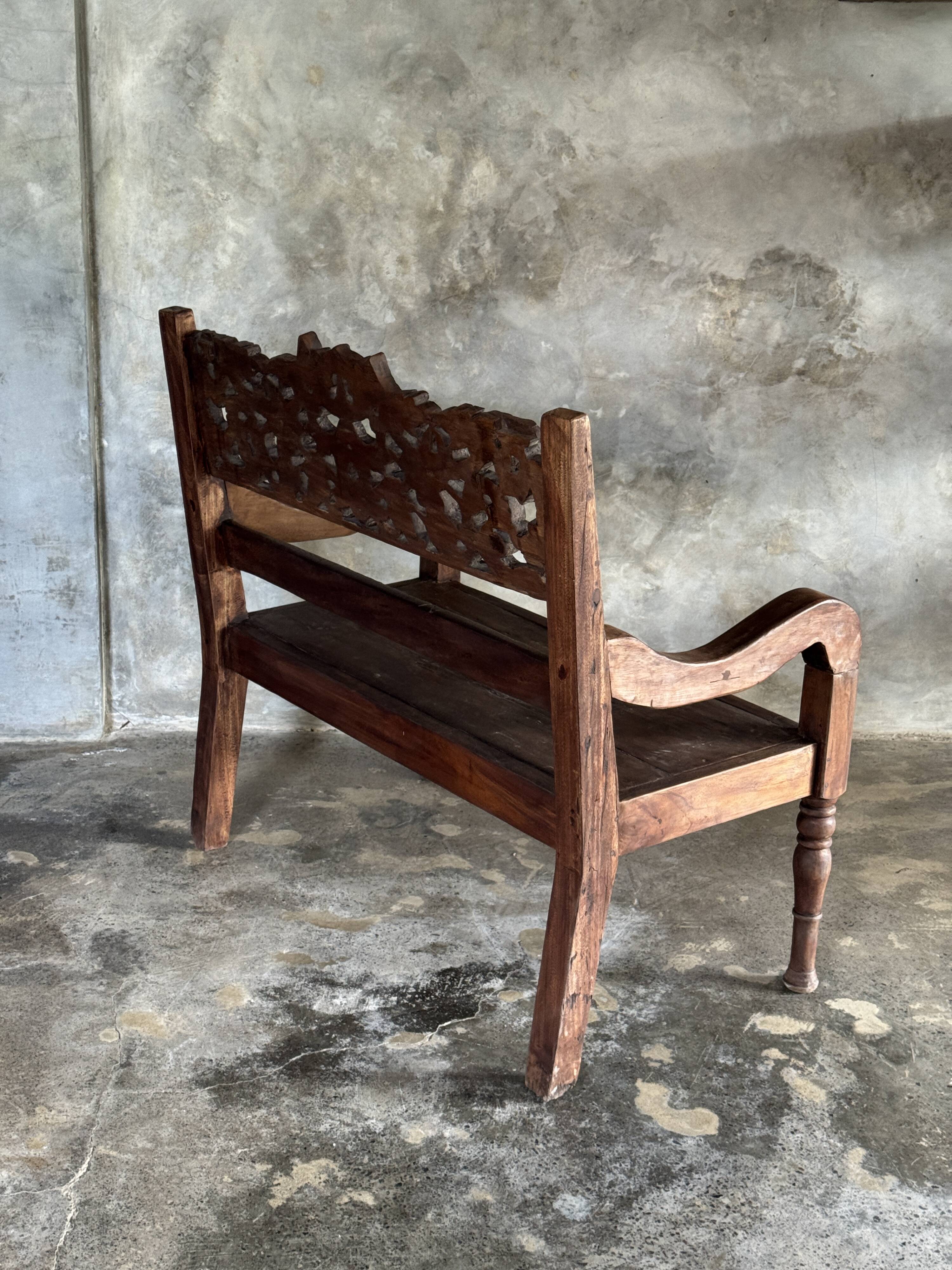 Small antique Indonesian bench in carved teak with plant and floral motifs.