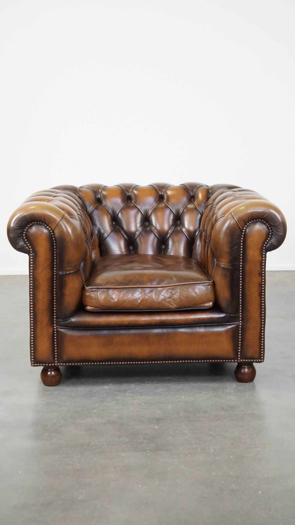 A well-maintained cowhide leather English Chesterfield armchair