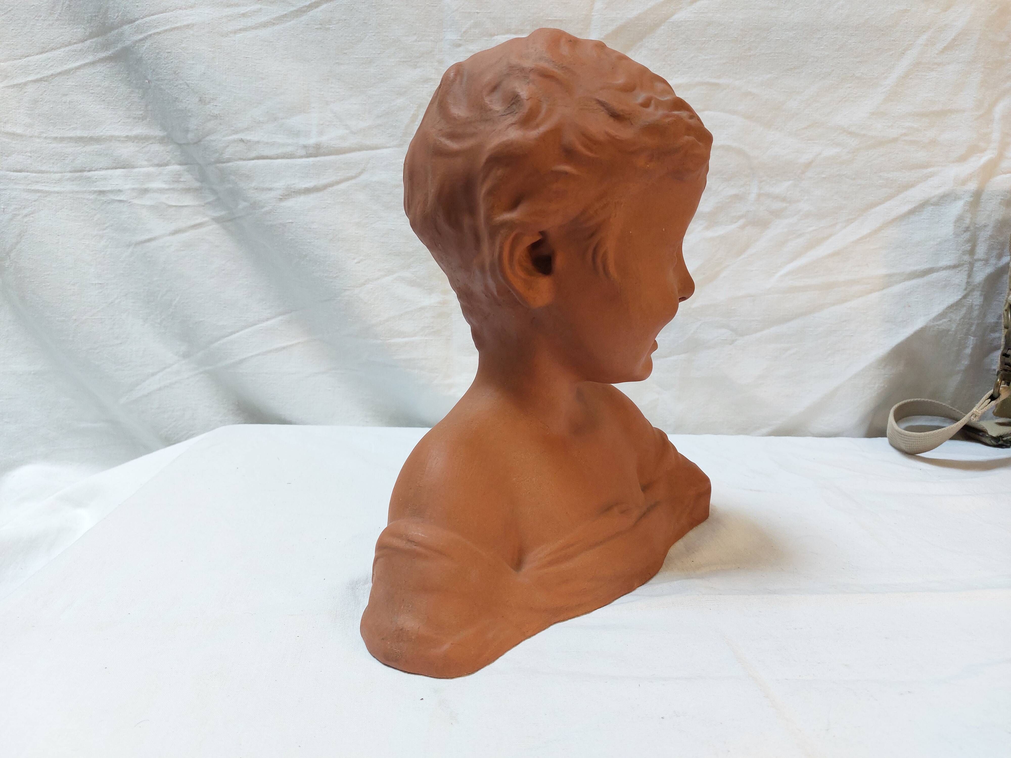 Terracotta bust of a smiling little boy.