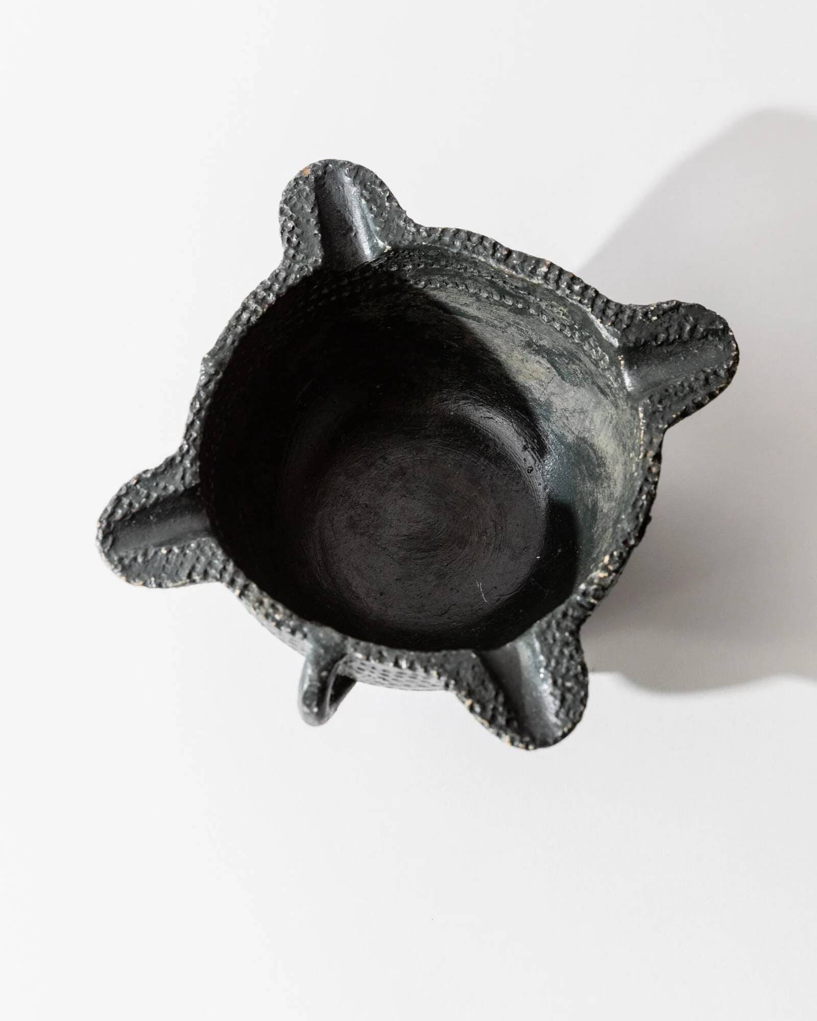Vintage ceramic ashtray from the 1960s, black, hand-sculpted texture, organic shape.