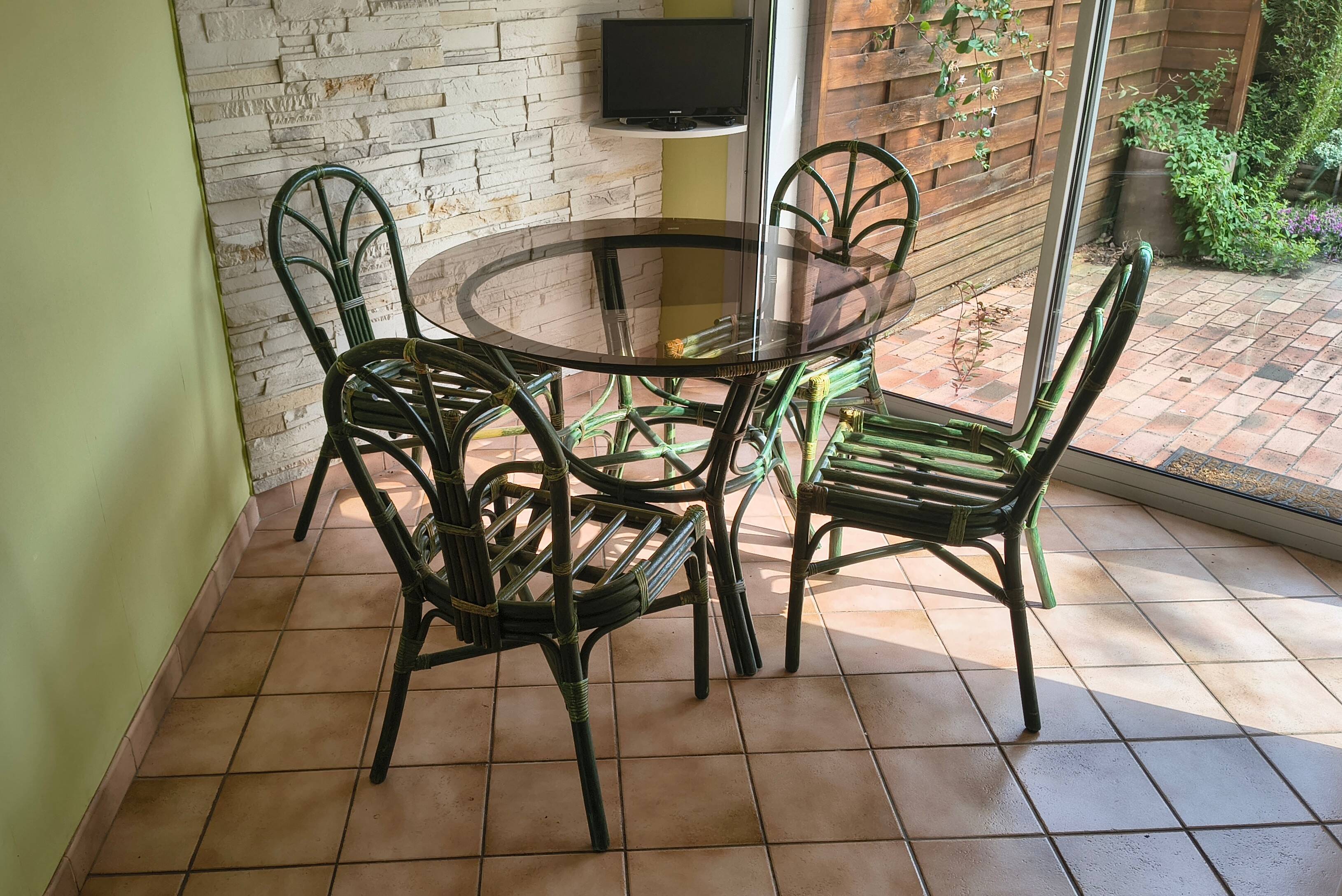 Round rattan table with glass top and 4 green rattan chairs.