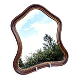 Antique wall mirror in carved wood with a wavy shape and a golden trim.