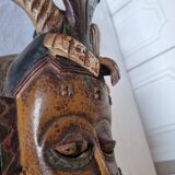 A large Senufo mask made of colored wood, decorated with an anthropomorphic figure